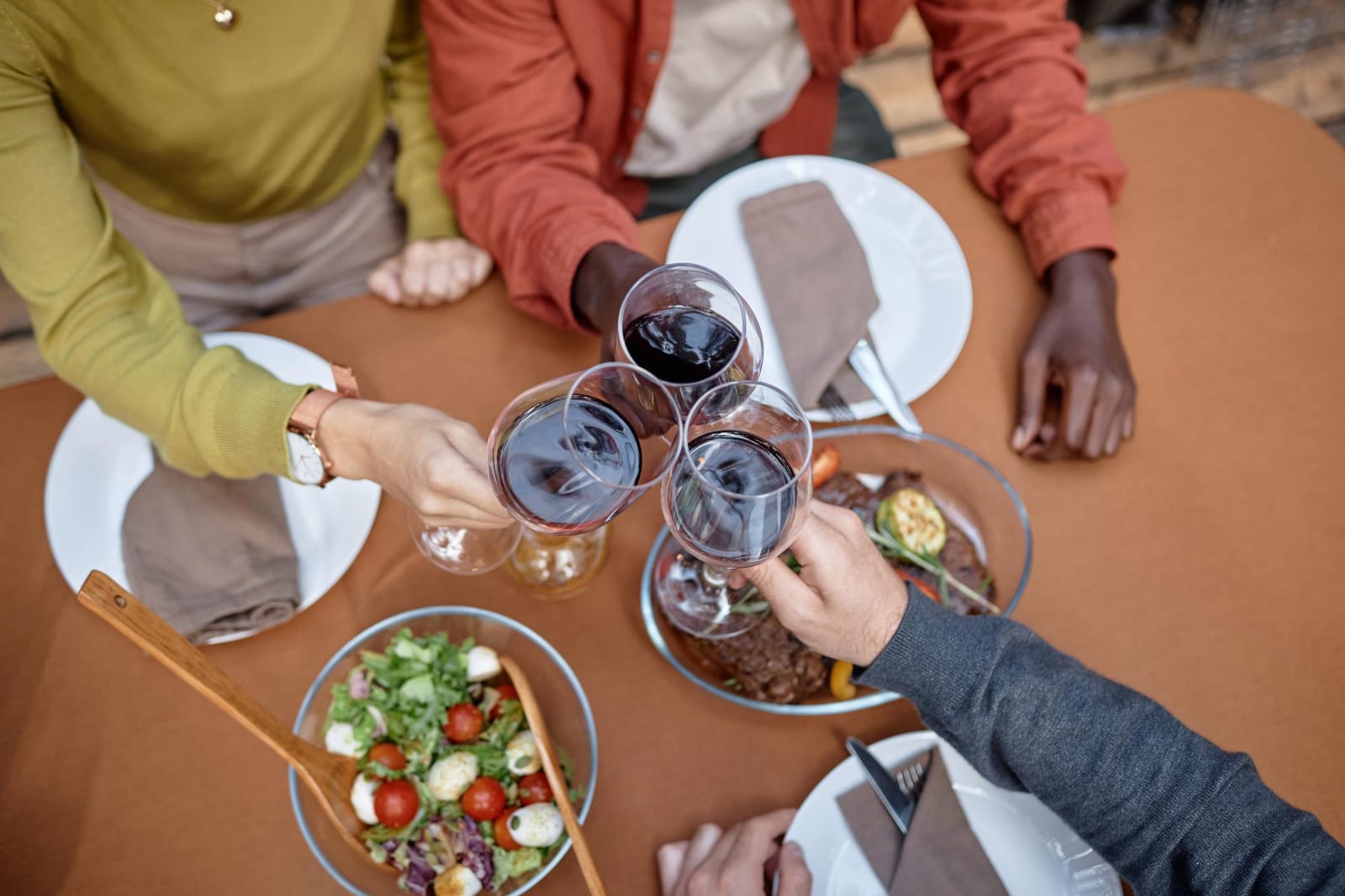 Amigos reunidos à mesa com carnes grelhadas e taças de vinho em um jantar de confraternização